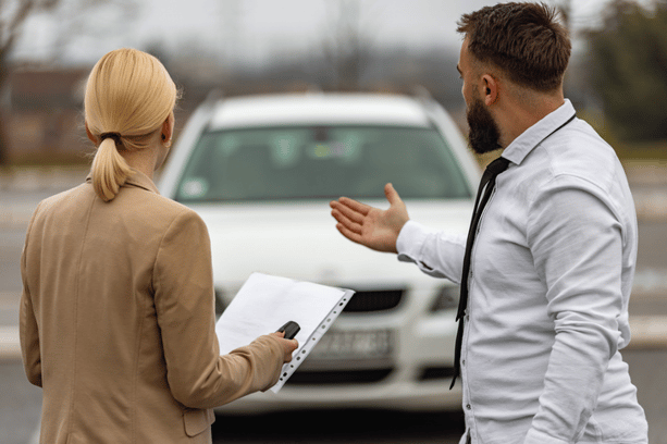 Man showing a white car to a woman holding a clipboard, likely during a car rental or sales inspection.