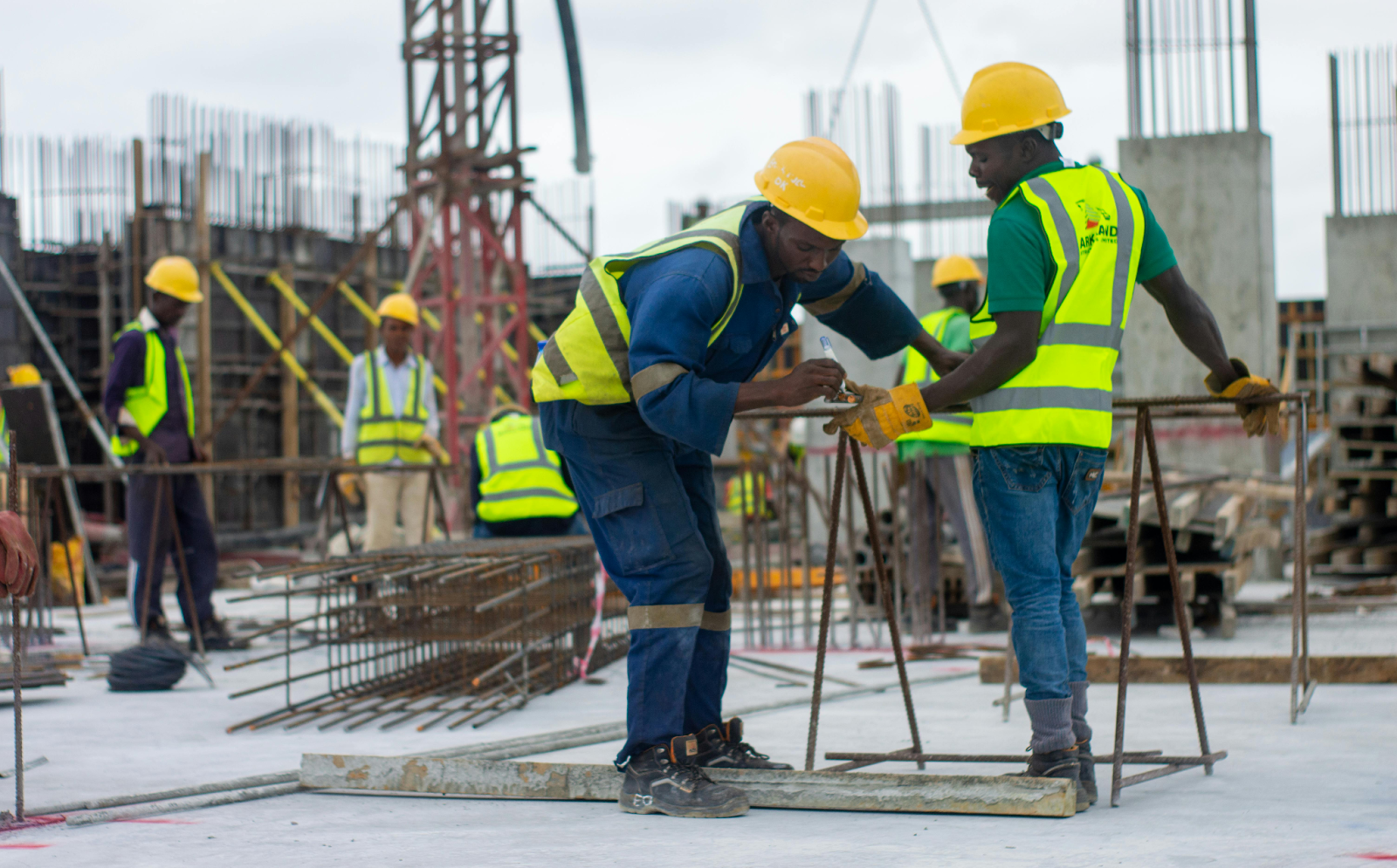 Construction workers in safety vests and helmets are inspecting a building site.